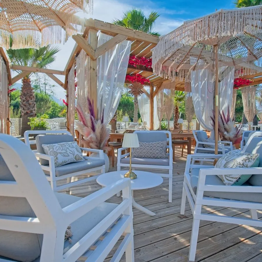 Terrasse en bois avec pergola, rideaux et fauteuils blancs d'un établissement client, prise de vue pour réseaux sociaux