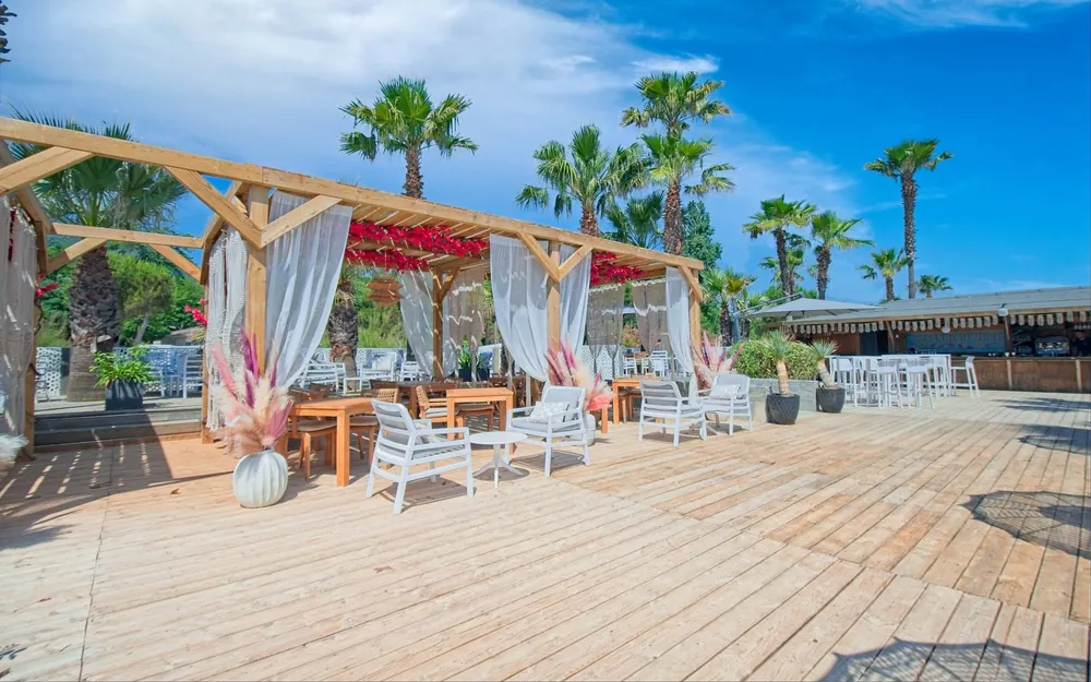 Terrasse de bar en bord de mer avec pergola, rideaux en macramé et fauteuils blancs